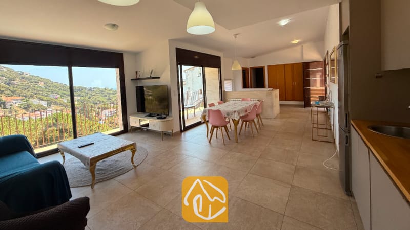 Vakantievilla's Costa Brava Spanje - Villa Sunny Beach - Open woon- en eetkamer in Villa Sunny Beach met tegelvloeren, grote glazen schuifdeuren en roze eetkamerstoelen.