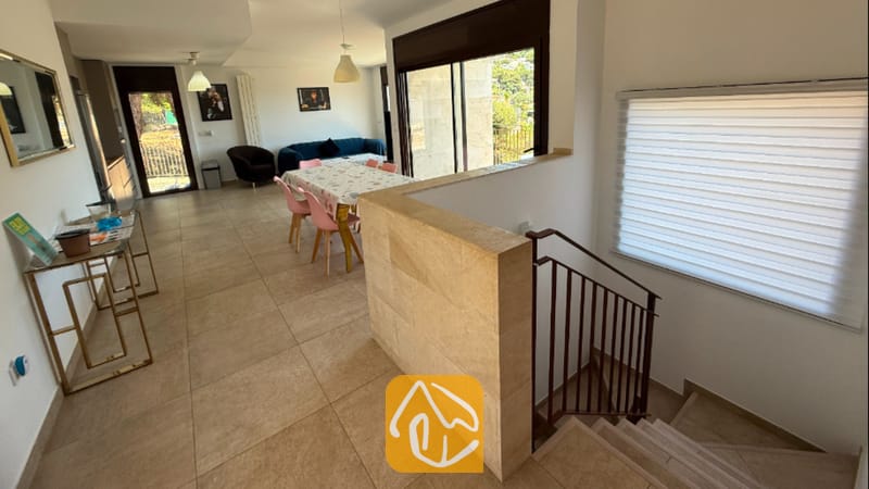 Vakantievilla's Costa Brava Spanje - Villa Sunny Beach - De open woon- en eetkamer van Villa Sunny Beach is voorzien van een trap met een stenen wand als afscheiding, tegelvloeren en roze eetkamerstoelen.
