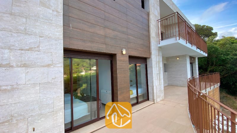 Vakantievilla's Costa Brava Spanje - Villa Sunny Beach - Buitenaanzicht van Villa Sunny Beach met een gebogen terras met bruine metalen leuningen, glazen schuifdeuren en een gevel van steen en hout.