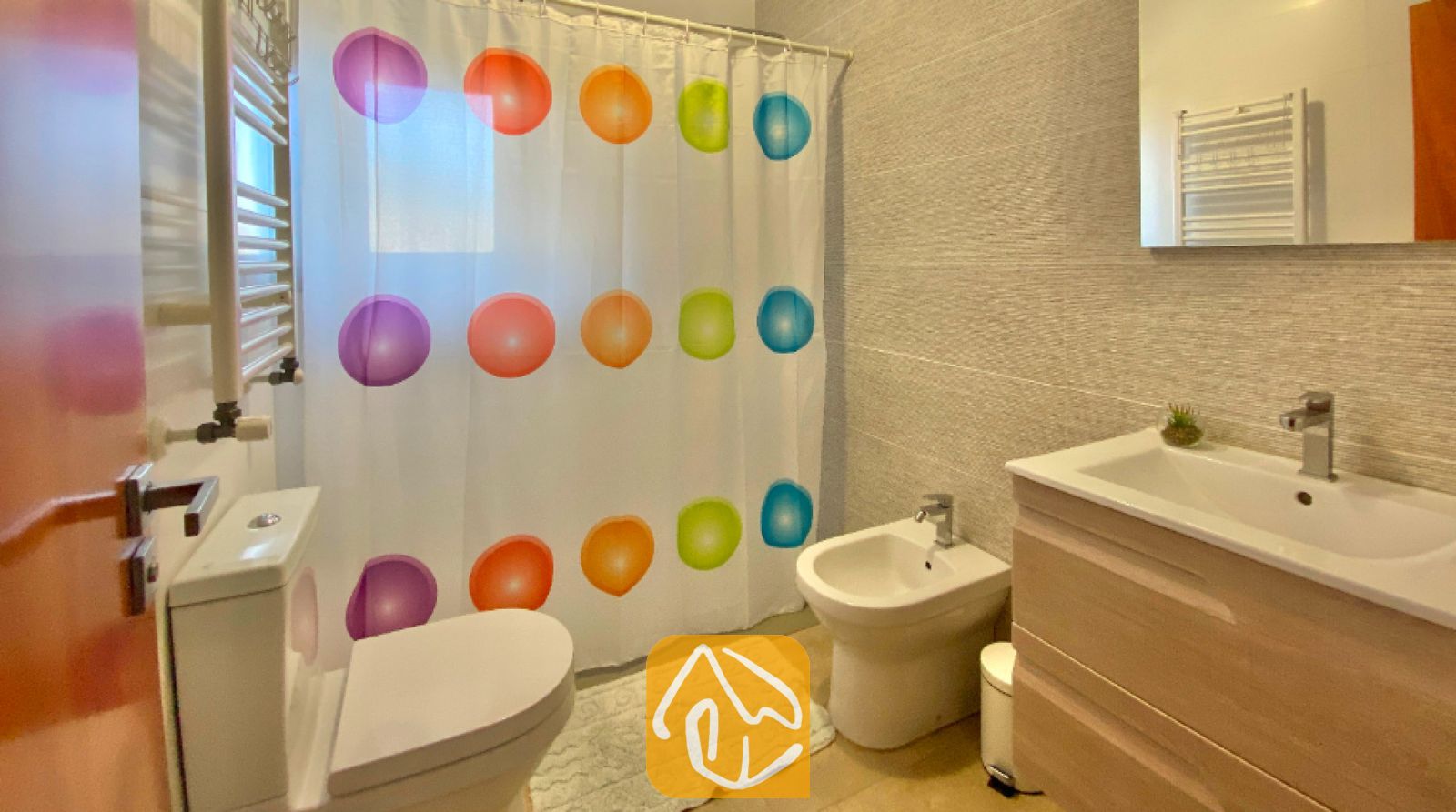 Vakantievilla's Costa Brava Spanje - Villa Sunny Beach - Badkamer met een witte wastafel met houten meubel, toilet, bidet en een wit douchevak met kleurrijke stippen.