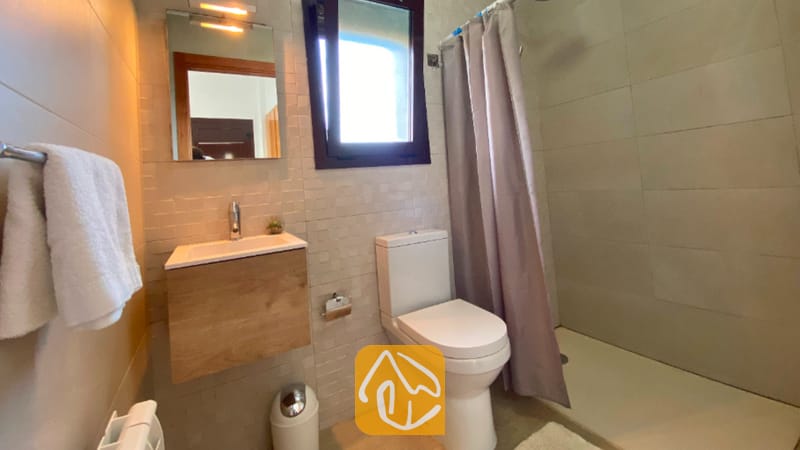 Villas de vacaciones Costa Brava España - Villa Sunny Beach - Baño moderno con mueble de tocador de madera, inodoro blanco y ducha a ras de suelo con cortina gris.