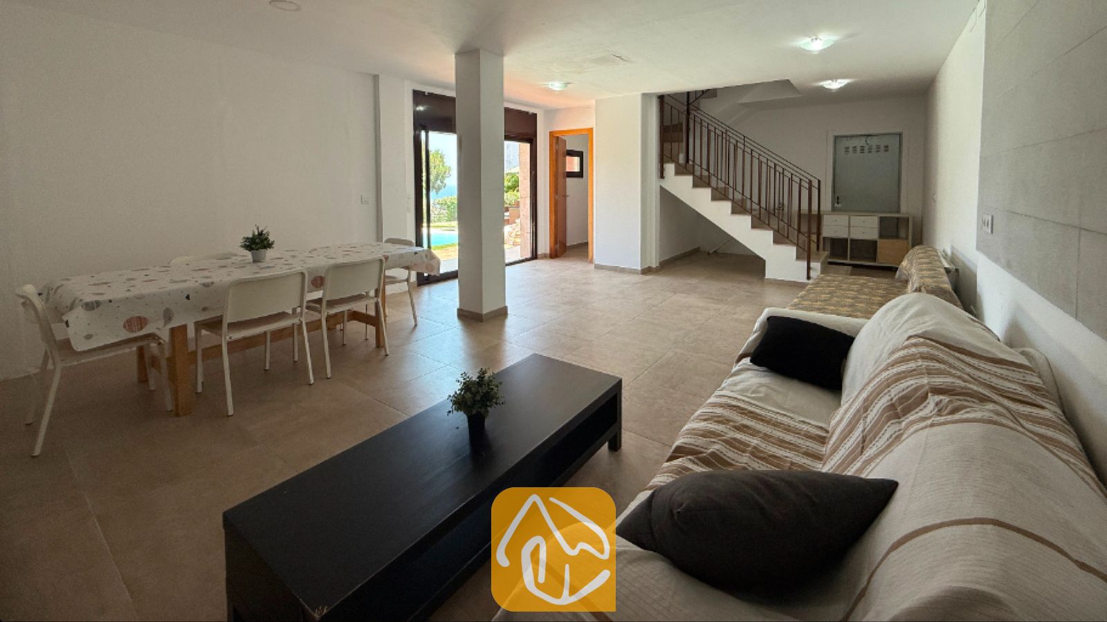 Vakantievilla's Costa Brava Spanje - Villa Sunny Beach - Ruime woon- en eetkamer in Villa Sunny Beach, voorzien van een bank met gestreepte hoezen, een donkere salontafel, een eettafel met stoelen en tegelvloeren.