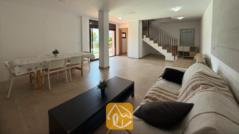 Vakantievilla's Costa Brava Spanje - Villa Sunny Beach - Ruime woon- en eetkamer in Villa Sunny Beach, voorzien van een bank met gestreepte hoezen, een donkere salontafel, een eettafel met stoelen en tegelvloeren.