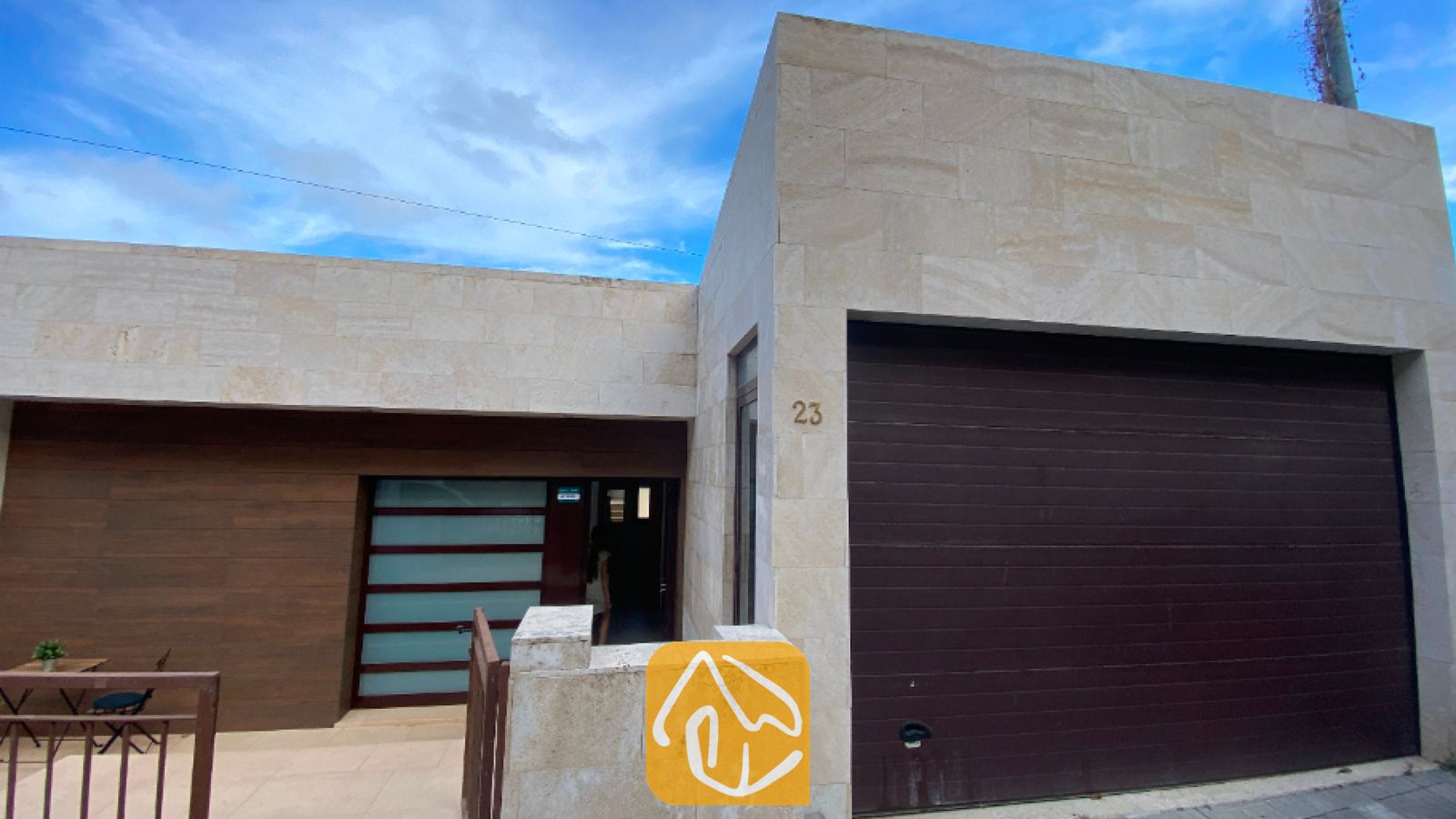 Vakantievilla's Costa Brava Spanje - Villa Sunny Beach - Moderne stenen buitenkant van Villa Sunny Beach, voorzien van een grote donkerbruine garagedeur, een gevel van lichte beige steentegels en een glazen voordeur.