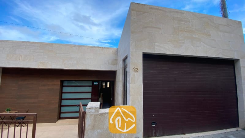Villas de vacaciones Costa Brava España - Villa Sunny Beach - Moderna fachada de piedra de Villa Sunny Beach que cuenta con un amplio garaje de puerta marrón oscura, un revestimiento de azulejos de piedra en tono beige claro y una entrada principal con paneles de cristal.