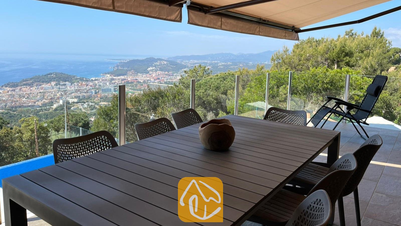 Vakantievilla's Costa Brava Spanje - Villa VistaMar - Overdekt buitenbuitenterras bij Villa VistaMar met een donkere houten tafel, gaasstoelen en een panoramisch uitzicht op zee en de kust.