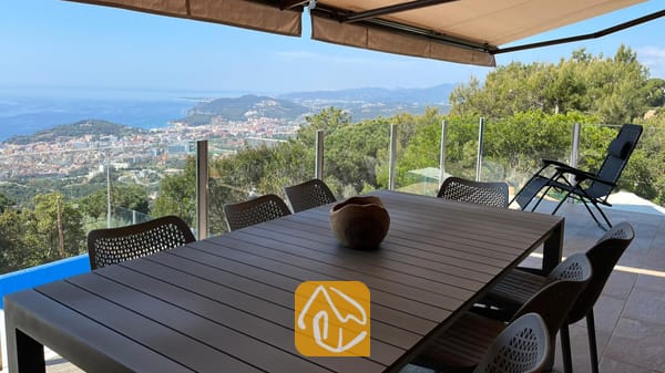 Vakantievilla's Costa Brava Spanje - Villa VistaMar - Overdekt buitenbuitenterras bij Villa VistaMar met een donkere houten tafel, gaasstoelen en een panoramisch uitzicht op zee en de kust.