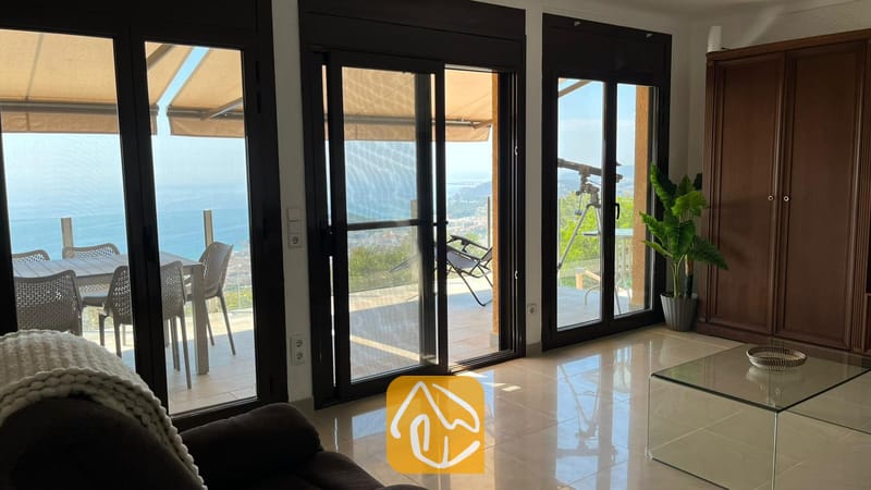 Vakantievilla's Costa Brava Spanje - Villa VistaMar - Interieur van de woonkamer in Villa VistaMar met grote glazen schuifpui die uitkomt op een buitenterras met uitzicht op zee, een tegelvloer en een glazen salontafel.