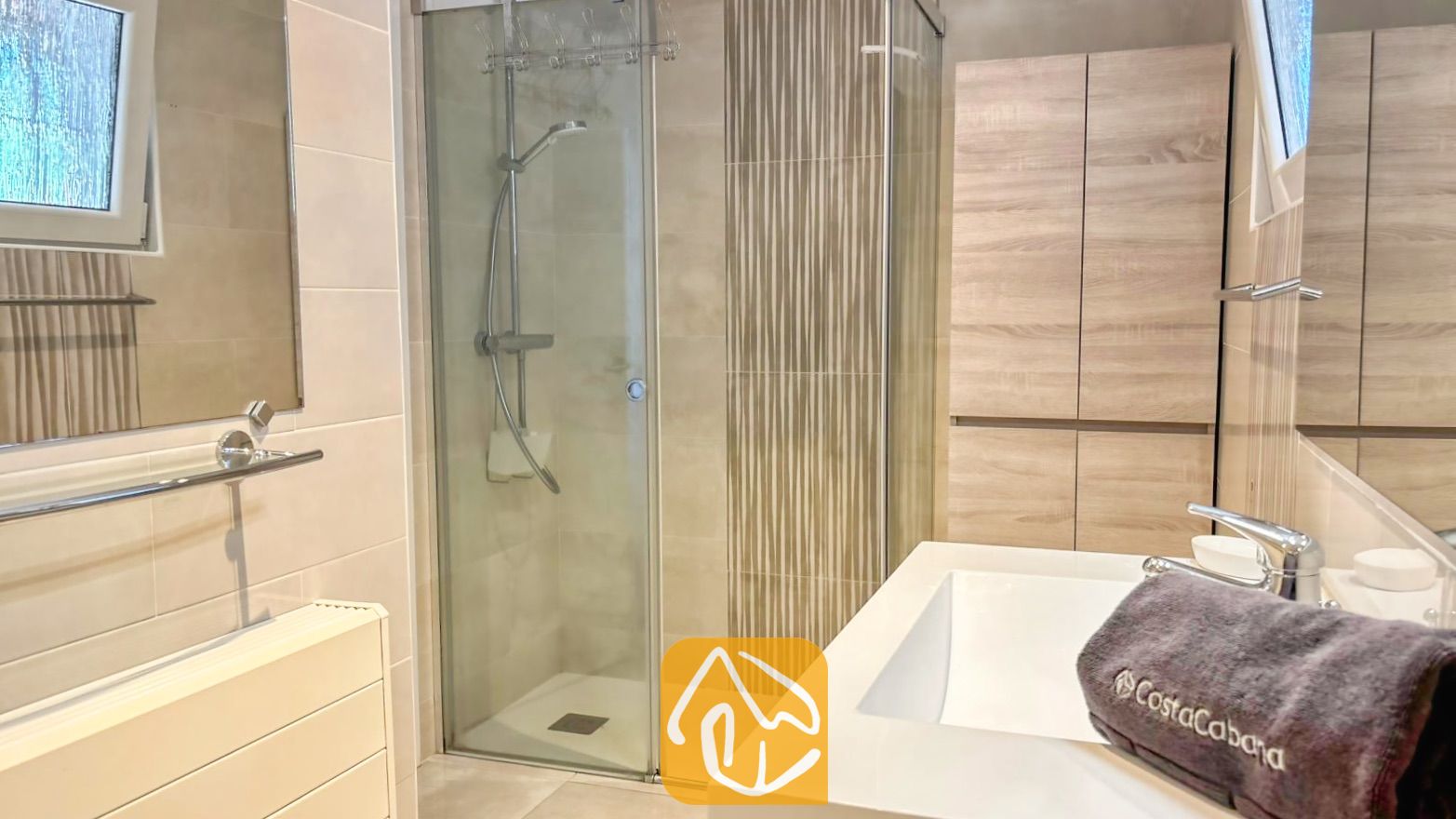 Vakantievilla's Costa Brava Spanje - Villa VistaMar - Moderne badkamer met een glazen inloopdouche, licht houten kasten en een wit wastafelblad met een grijze handdoek.