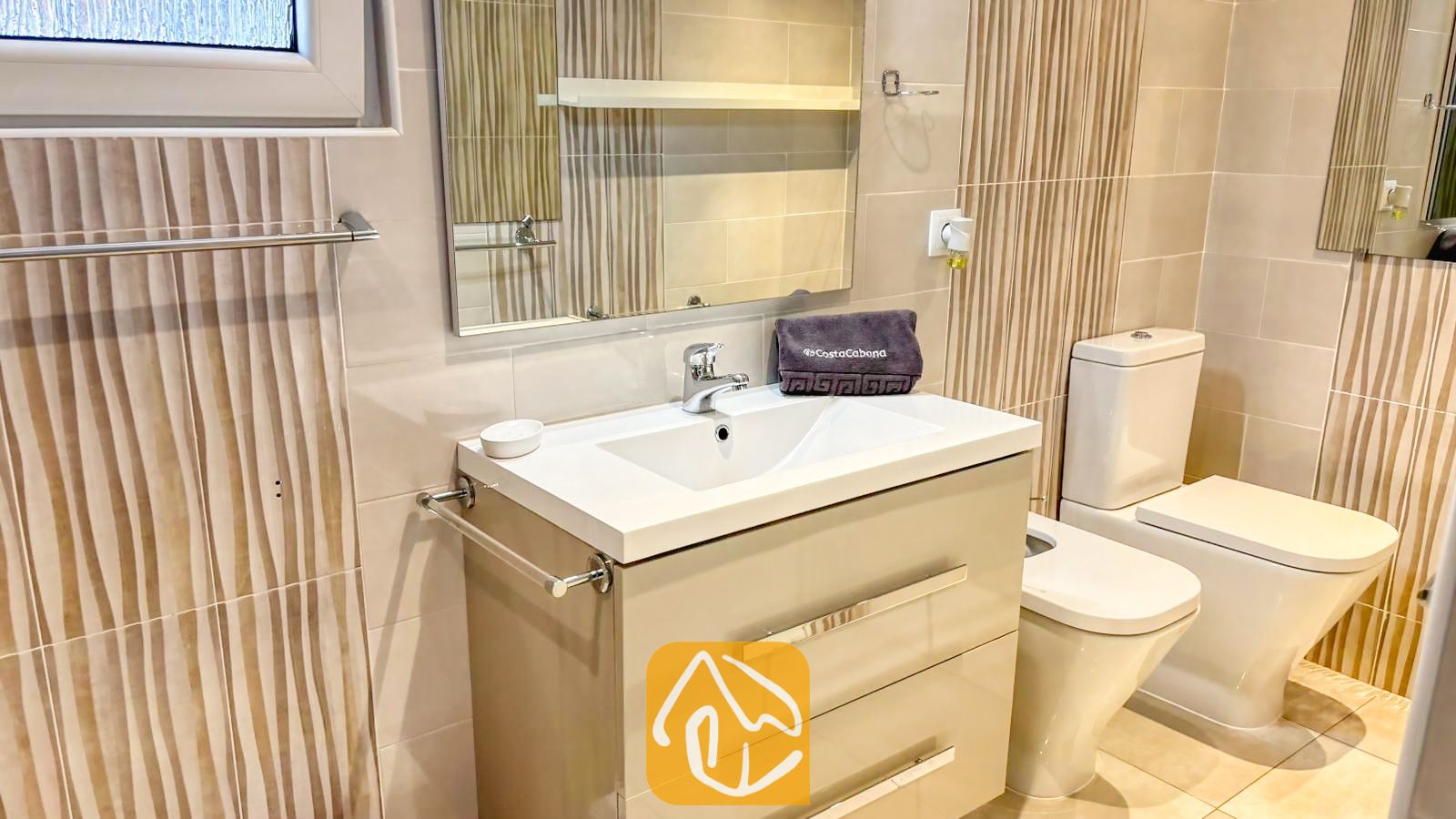 Vakantievilla's Costa Brava Spanje - Villa VistaMar - Moderne badkamer met een wit porseleinen wastafelmeubel met chroombeslag, beige gestreepte wandtegels en een wit toilet.