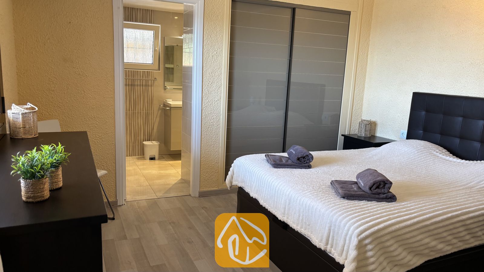 Vakantievilla's Costa Brava Spanje - Villa VistaMar - Slaapkamer voorzien van een tweepersoonsbed met opgevouwen grijze handdoeken, een schuifdeurenkast en een open doorgang naar een en-suite badkamer met betegelde muren.