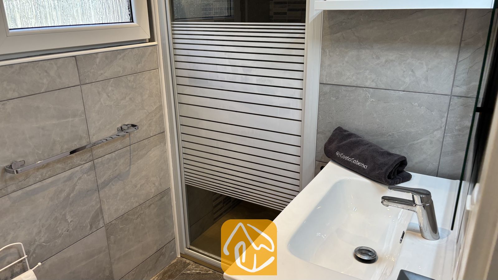 Vakantievilla's Costa Brava Spanje - Villa VistaMar - Modern badkamerinterieur met grijze natuurstenen tegels, een wit keramische wastafel met een chroomkraan en een matglas douchedeur.