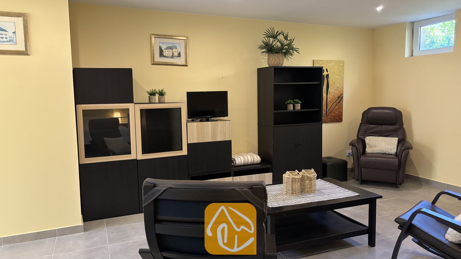 Vakantievilla's Costa Brava Spanje - Villa VistaMar - Woonkamer met zwarte kasten, donkere lederen fauteuils en een lage salontafel tegen gele muren in Villa VistaMar