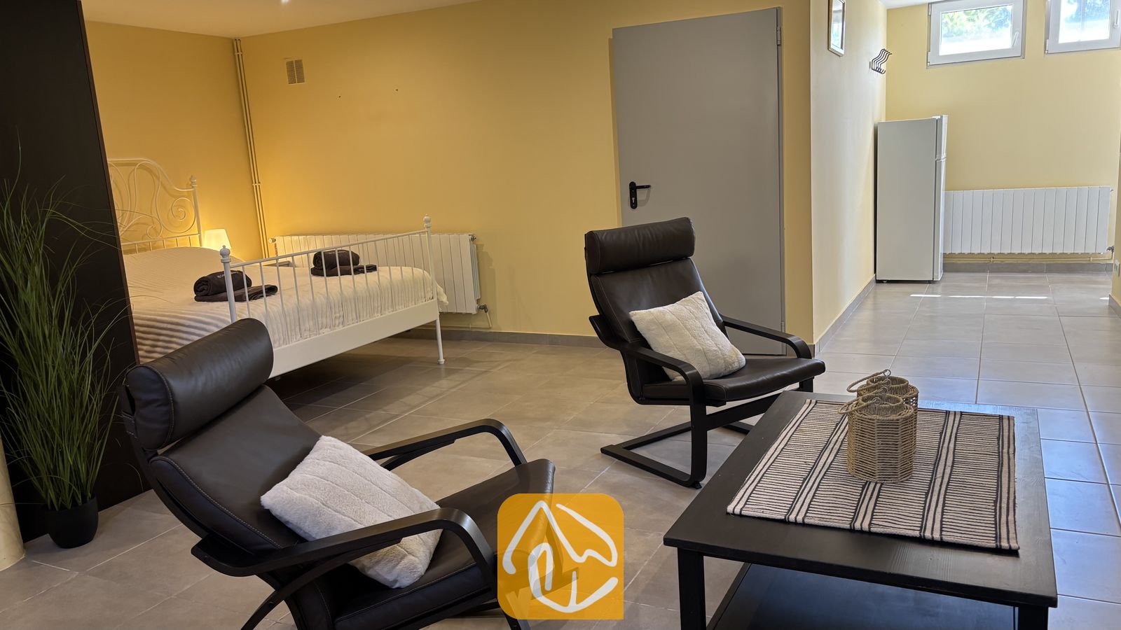 Vakantievilla's Costa Brava Spanje - Villa VistaMar - Ruim interieur in Villa VistaMar met twee donkere fauteuils van leer, een zwarte salontafel en een wit metalen bed tegen gele muren.