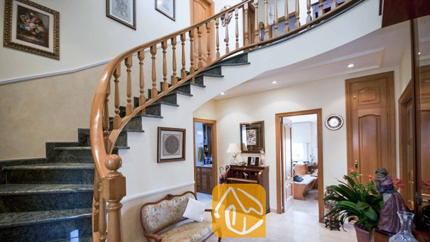 Vakantievilla's Costa Brava Spanje - Villa Mercedes Fenals - Geboogde marmeren trap met houten leuning in de hal van Villa Mercedes Fenals, voorzien van ingelijste kunstwerken en houten deuren