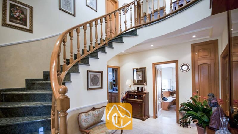 Ferienhäuser Costa Brava Spanien - Villa Mercedes Fenals - Geschwungene Marmortreppe mit Holzhandlauf im Flur der Villa Mercedes Fenals, akzentuiert durch gerahmte Kunstwerke und Holztüren