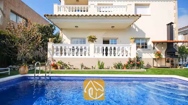 Vakantievilla's Costa Brava Spanje - Villa Mercedes Fenals - Privézwembad met helderblauw water voor de buitenkant van Villa Mercedes Fenals, voorzien van balkons met witte balustrades, een gazon en een stenen barbecue in de buitenlucht.