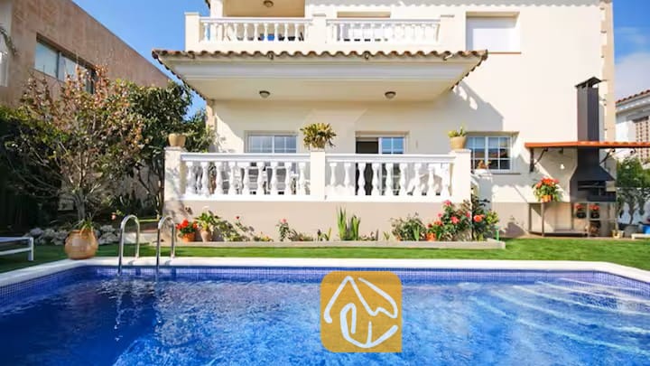 Vakantievilla's Costa Brava Spanje - Villa Mercedes Fenals - Privézwembad met helderblauw water voor de buitenkant van Villa Mercedes Fenals, voorzien van balkons met witte balustrades, een gazon en een stenen barbecue in de buitenlucht.