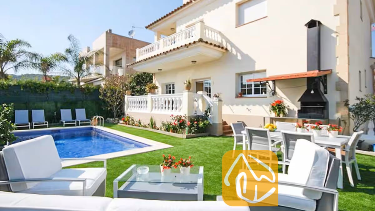 Vakantievilla's Costa Brava Spanje - Villa Mercedes Fenals - Buitenaanzicht van Villa Mercedes Fenals, met een zwembad, gazon, witte tuinstoelen en een ingebouwde buitenbarbecue tegen de crèmekleurige gevel.