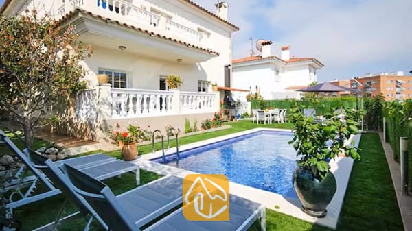 Vakantievilla's Costa Brava Spanje - Villa Mercedes Fenals - Buitenaanzicht van Villa Mercedes Fenals met een rechthoekig zwembad omringd door grijs ligbedden, een gazon, potplanten en de witte gevel van de villa met meerdere verdiepingen op de achtergrond.