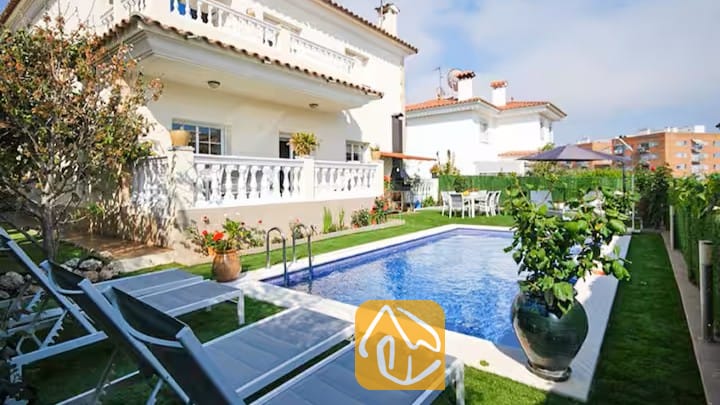 Vakantievilla's Costa Brava Spanje - Villa Mercedes Fenals - Buitenaanzicht van Villa Mercedes Fenals met een rechthoekig zwembad omringd door grijs ligbedden, een gazon, potplanten en de witte gevel van de villa met meerdere verdiepingen op de achtergrond.