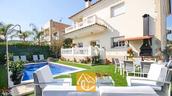 Vakantievilla's Costa Brava Spanje - Villa Mercedes Fenals - Buitenaanzicht van Villa Mercedes Fenals met een eigen zwembad, een groen gazon, witte 
tuinmeubelen en een aangebouwde barbecuehoek.