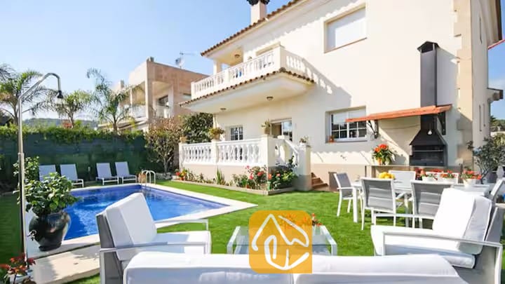 Vakantievilla's Costa Brava Spanje - Villa Mercedes Fenals - Buitenaanzicht van Villa Mercedes Fenals met een eigen zwembad, een groen gazon, witte 
tuinmeubelen en een aangebouwde barbecuehoek.