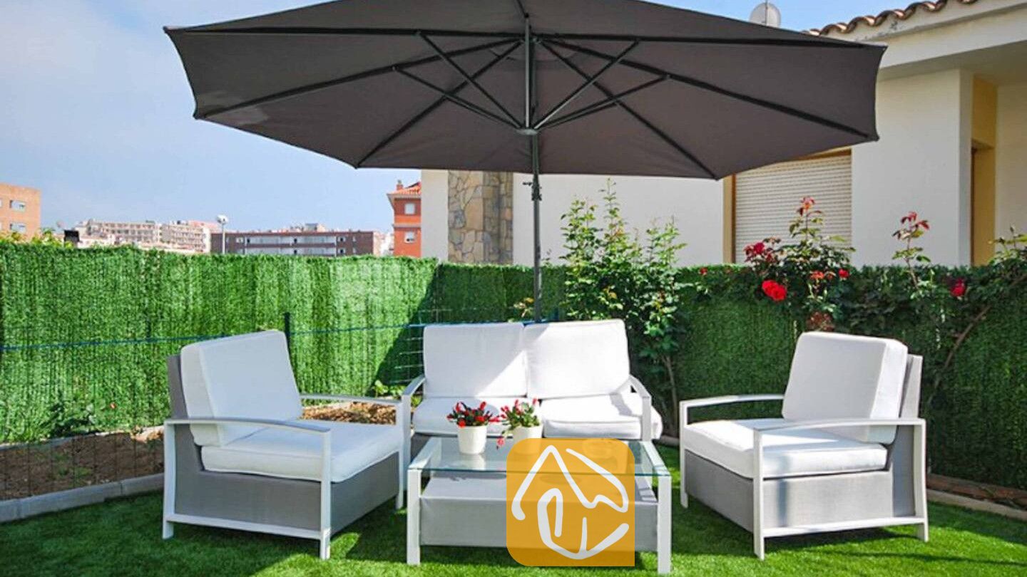 Vakantievilla's Costa Brava Spanje - Villa Mercedes Fenals - Loungehoek op het buitenterras van Villa Mercedes Fenals, voorzien van een grijze parasol, wit gekussende fauteuils, een bijpassende bank en een salontafel met glazen blad op kunstgras.