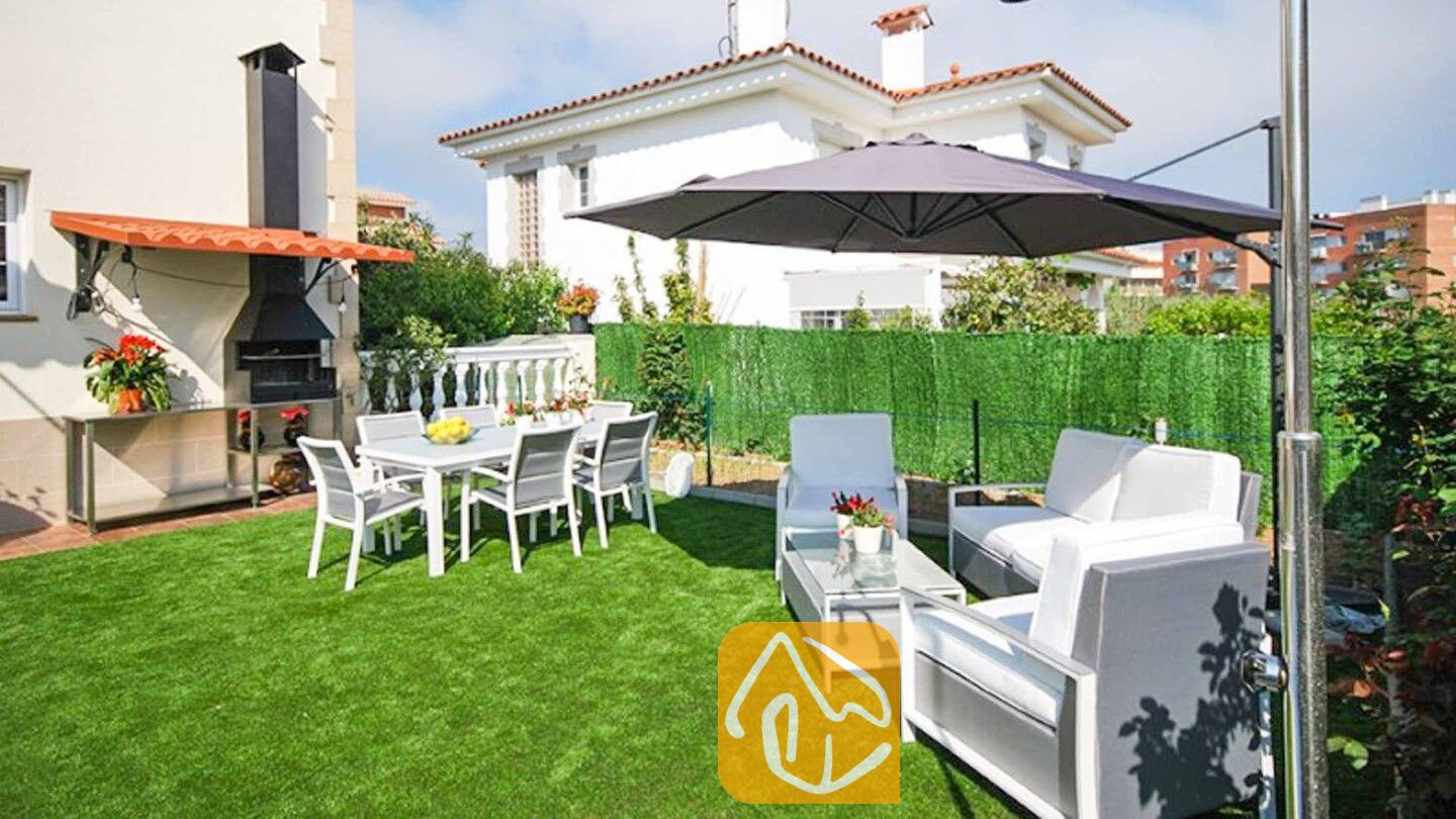 Vakantievilla's Costa Brava Spanje - Villa Mercedes Fenals - Eetgedeelte buiten en loungesets op het kunstgrasveld bij Villa Mercedes Fenals, voorzien van een zwarte stenen barbecue en een grote grijze parasol.