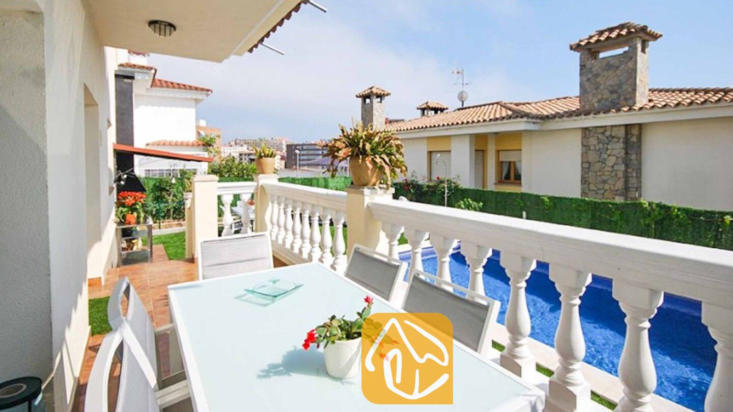 Vakantievilla's Costa Brava Spanje - Villa Mercedes Fenals - Balkonterras van Villa Mercedes Fenals met een witte eettafel en stoelen, uitkijkend over een zwembad en nabijgelegen gebouwen.