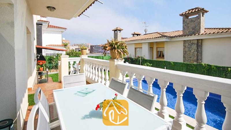 Vakantievilla's Costa Brava Spanje - Villa Mercedes Fenals - Balkonterras van Villa Mercedes Fenals met een witte eettafel en stoelen, uitkijkend over een zwembad en nabijgelegen gebouwen.