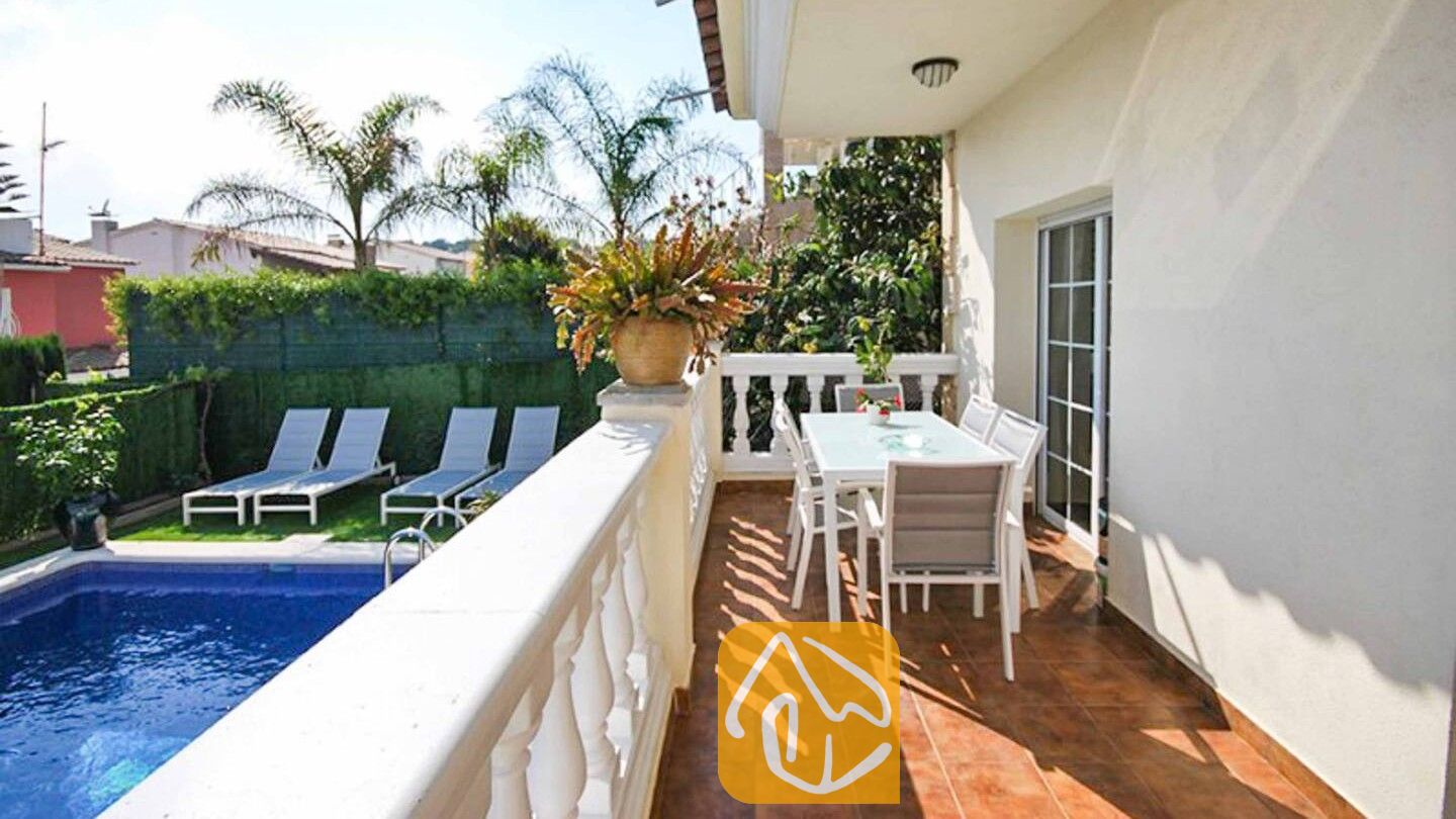 Vakantievilla's Costa Brava Spanje - Villa Mercedes Fenals - Balkon van Villa Mercedes Fenals met een eettafel en stoelen buiten, uitkijkend over het zwembad en de palmbomen beneden.