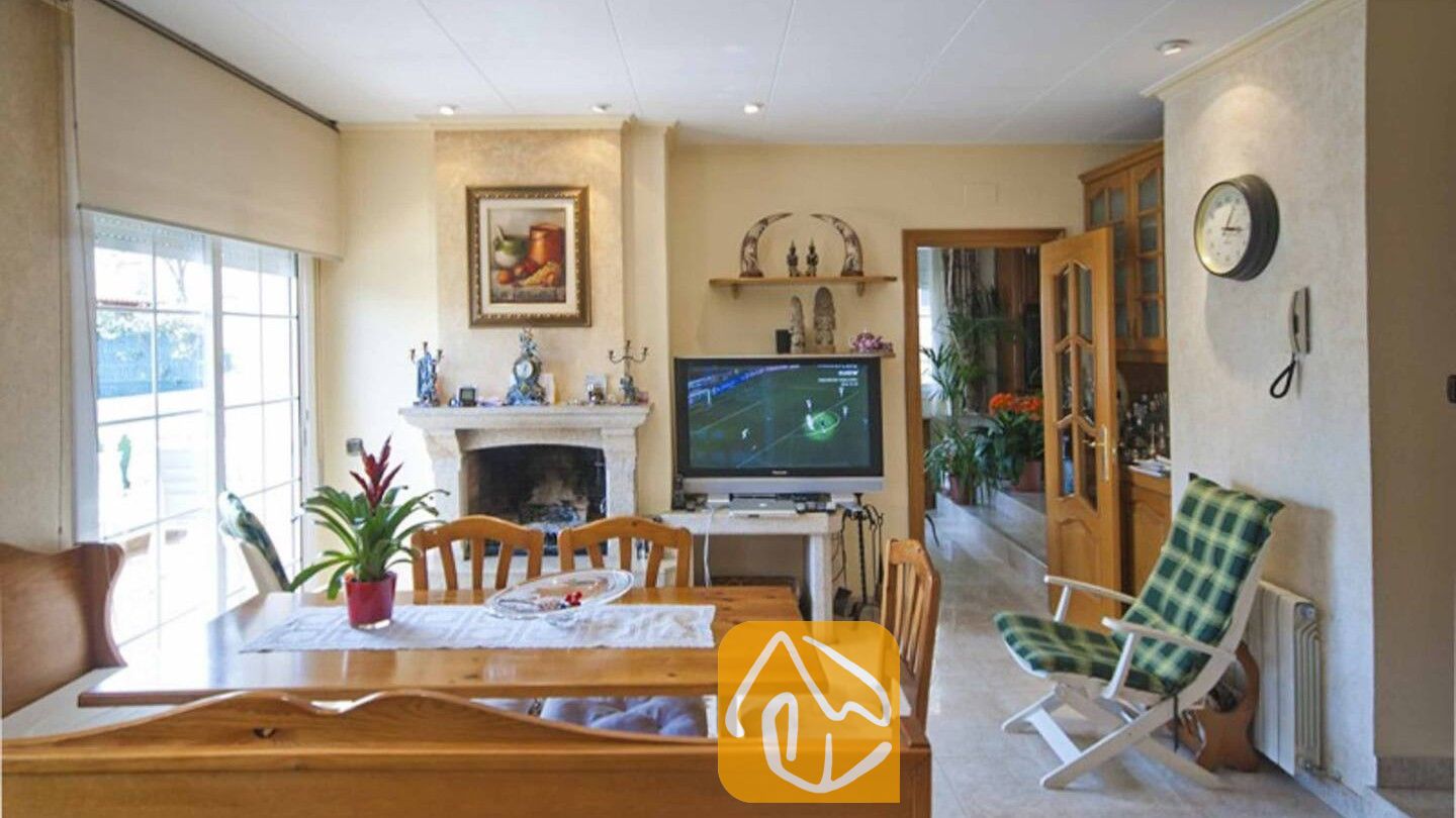 Vakantievilla's Costa Brava Spanje - Villa Mercedes Fenals - Woonkamer en eethoek voorzien van een houten eettafel, stenen open haard en televisie bij Villa Mercedes Fenals.