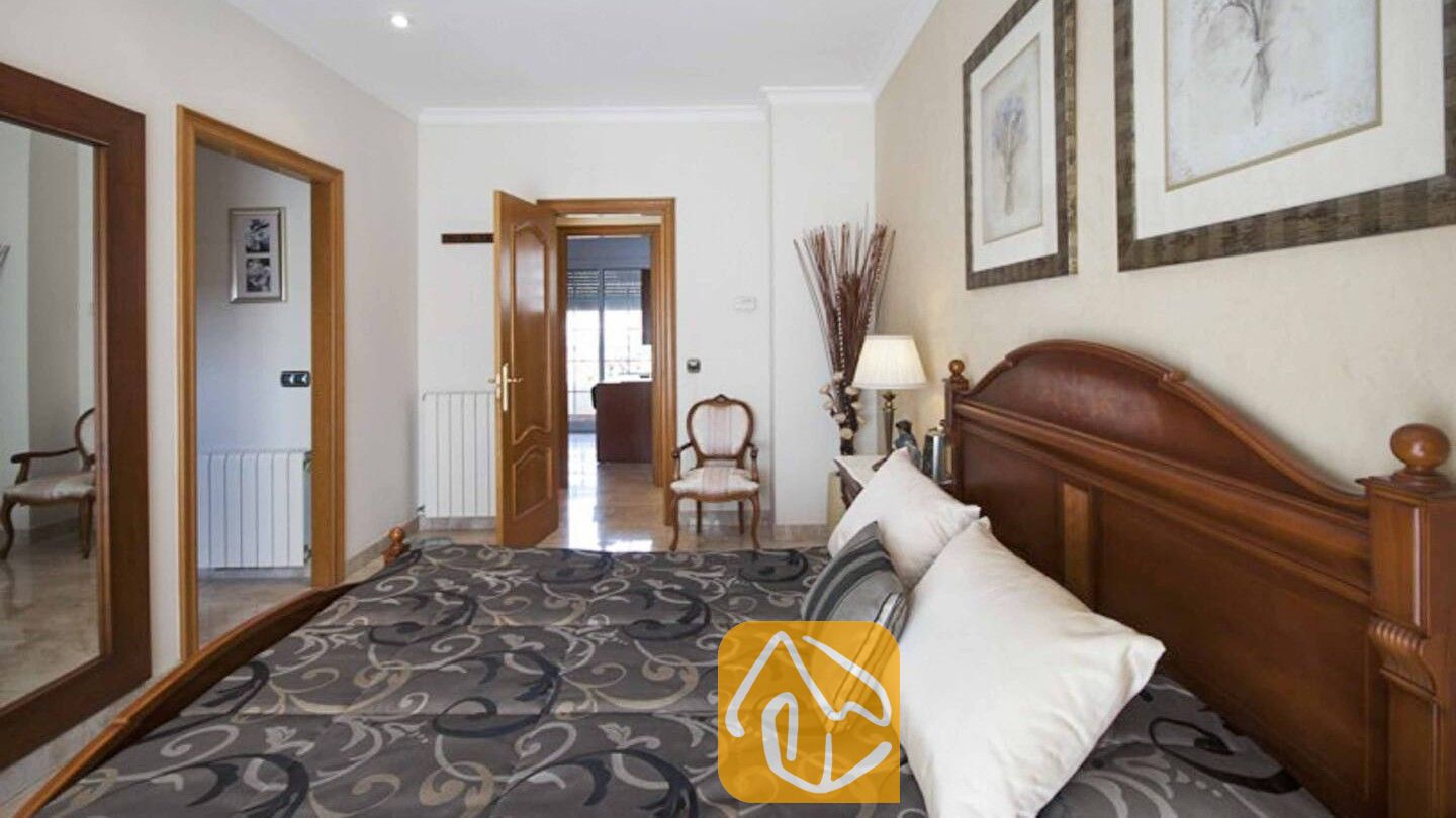 Vakantievilla's Costa Brava Spanje - Villa Mercedes Fenals - Slaapkamer met een donkerhouten hoofdbord, beddengoed met een motief, witte kussens en ingelijste kunst aan beige muren.