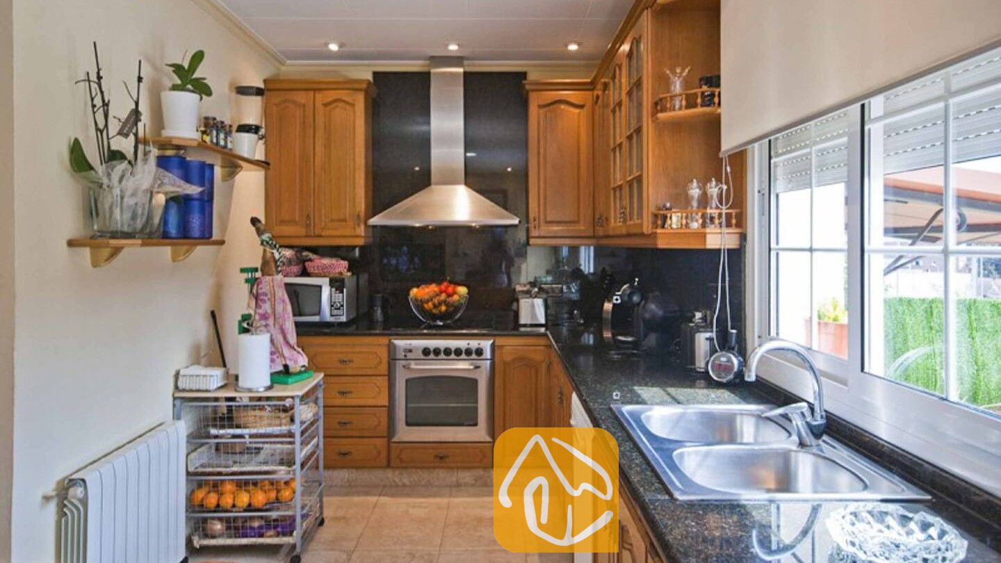Vakantievilla's Costa Brava Spanje - Villa Mercedes Fenals - Keuken met houten kasten, donkere granieten aanrechtbladen, een RVS oven en een dubbele spoelbak onder een raam.