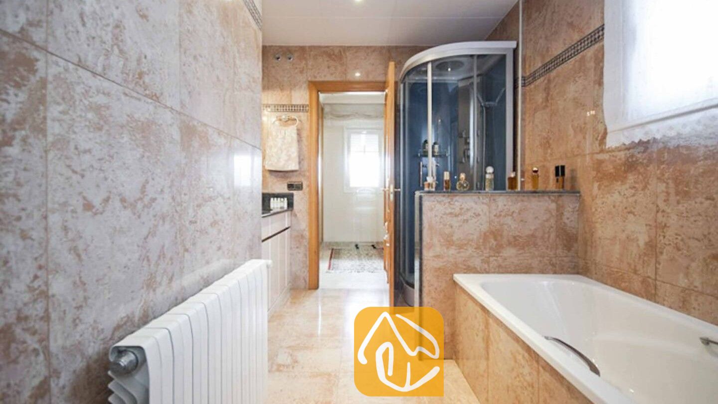 Vakantievilla's Costa Brava Spanje - Villa Mercedes Fenals - Badkamer voorzien van beige marmeren wandtegels, een wit ligbad en een glazen hoekdouchecabine.