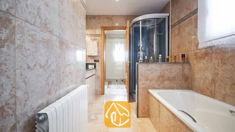 Ferienhäuser Costa Brava Spanien - Villa Mercedes Fenals - Badezimmer mit beige marmorierten Fliesenwänden, einer weißen Badewanne und einer gläsernen Eckdusche.