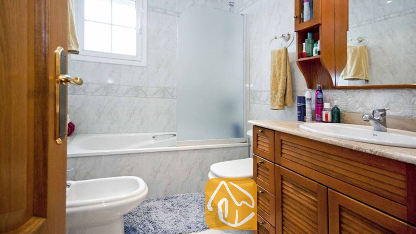 Vakantievilla's Costa Brava Spanje - Villa Mercedes Fenals - Badkamer voorzien van een houten badkamermeubel met een marmeren blad, een ligbad met een matglazen wand en witte wandtegels.