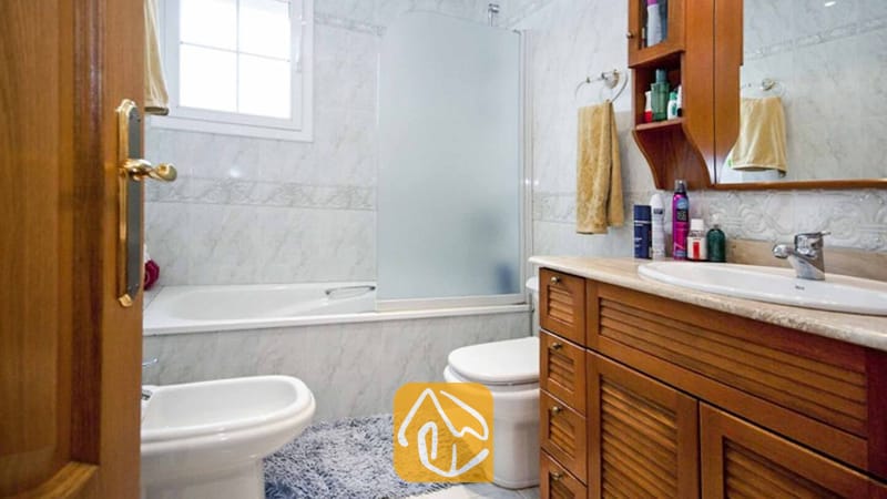 Ferienhäuser Costa Brava Spanien - Villa Mercedes Fenals - Badezimmer mit einem Waschtisch aus Holz und Marmorplatte, einer Badewanne mit Milchglaswand sowie weißen Wandfliesen.