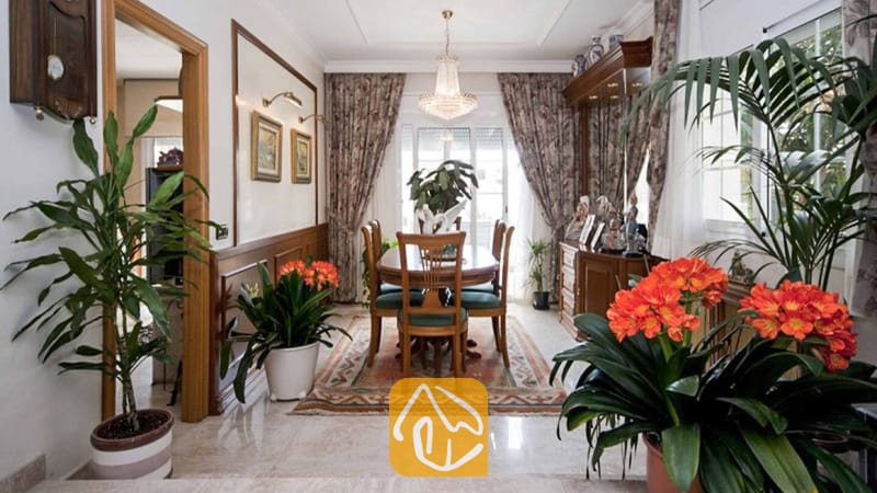 Ferienhäuser Costa Brava Spanien - Villa Mercedes Fenals - Das Esszimmer der Villa Mercedes Fenals besticht durch einen Holztisch mit Stühlen, einen Kristalllüster, gemusterte Vorhänge und Topfpflanzen, die den Blick kunstvoll einrahmen.