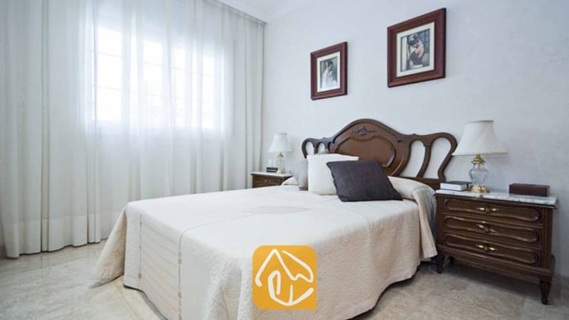 Ferienhäuser Costa Brava Spanien - Villa Mercedes Fenals - Schlafzimmer mit dunklem Holzkopfteil, passenden Nachttischen und hell gemusterter Bettwäsche in der Villa Mercedes Fenals