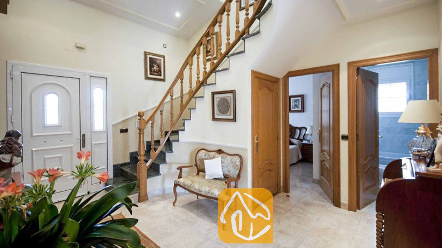 Vakantievilla's Costa Brava Spanje - Villa Mercedes Fenals - Lichte entree met een houten trap met spijlen, marmeren tegelvloeren en open deuropeningen bij Villa Mercedes Fenals.
