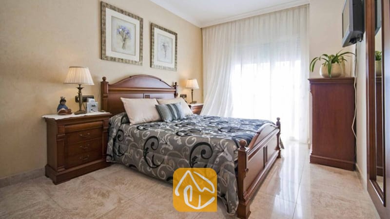 Ferienhäuser Costa Brava Spanien - Villa Mercedes Fenals - Schlafzimmer mit dunklem Holzbettgestell, gemusterter grauer Bettdecke und passenden Nachttischen mit Lampen.