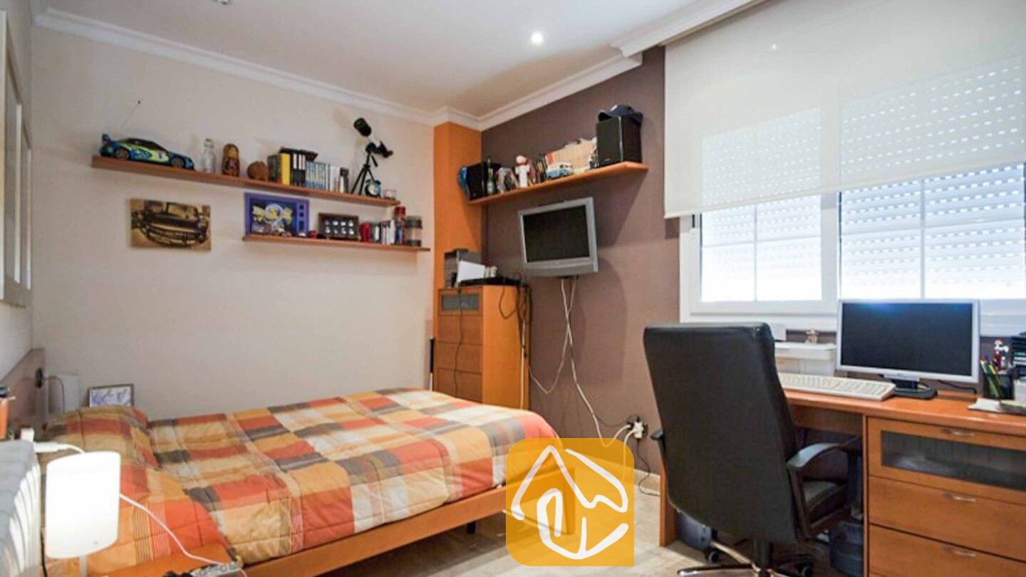 Vakantievilla's Costa Brava Spanje - Villa Mercedes Fenals - Slaapkamer met een eenpersoonsbed voorzien van een oranje geruite deken, houten planken met speelgoed en boeken, en een bureau met een computer.